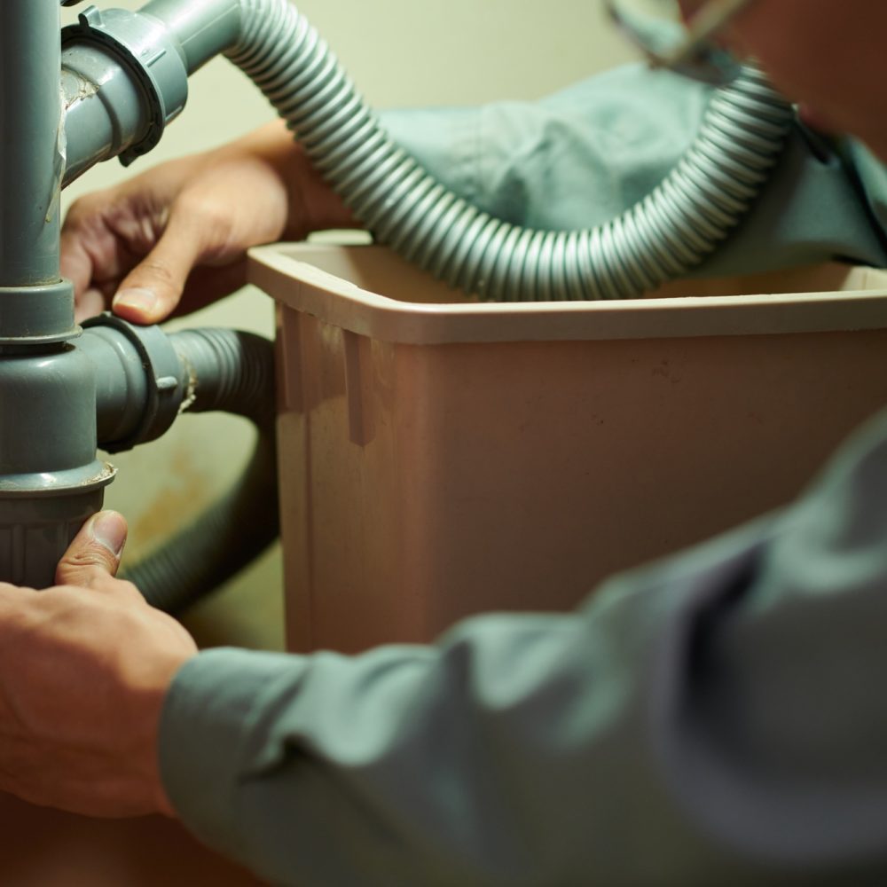 home service worker cleaning plastic pipe under kitchen sink