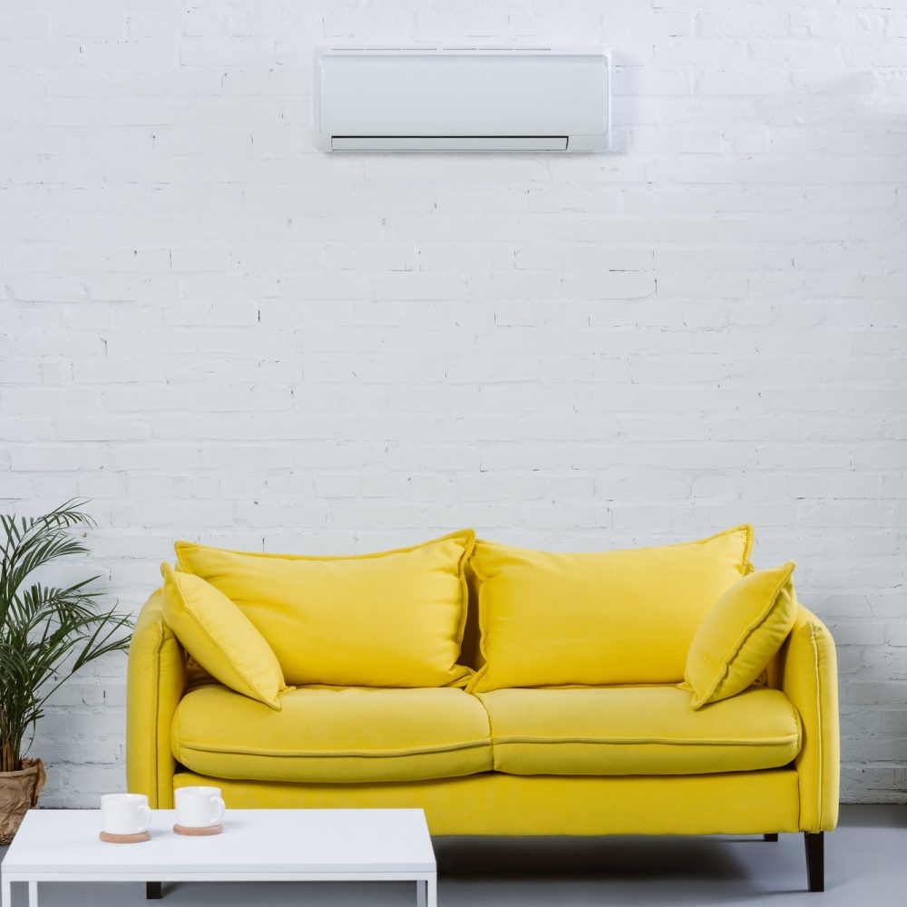 interior of modern living room with yellow couch and air conditioner hanging on white wall interior of modern living room with yellow couch and air conditioner hanging on white wall