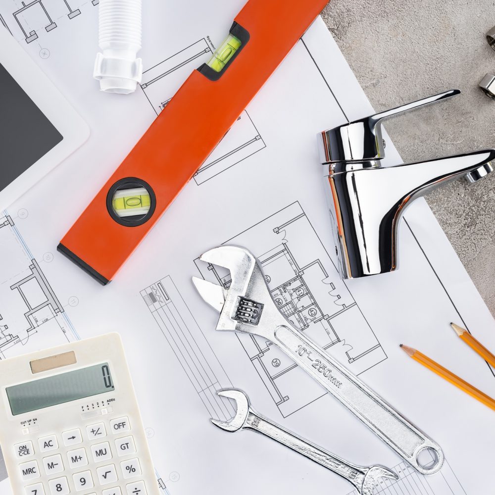 top view of building plan with plumbing tools and calculator on concrete surface top view of building plan with plumbing tools and calculator on concrete surface